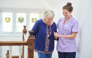 Carer assisting elderly woman up stairs